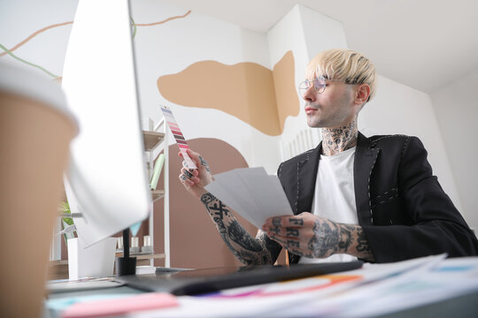 Tattooed graphic designer working with paint palettes at table in office