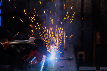 During welding process at this workplace, sparks are lighting smoke in factory where worker is welding steel