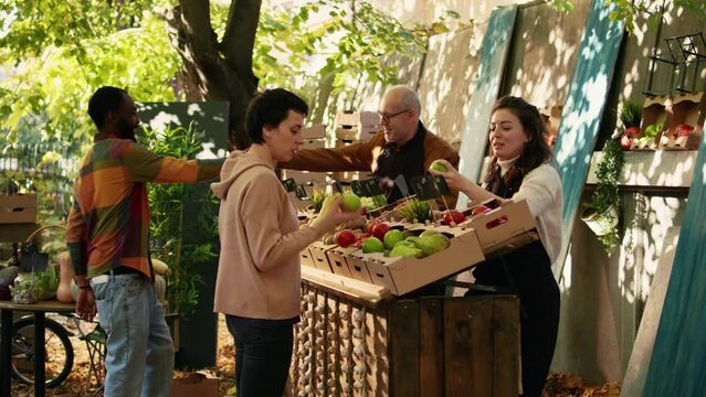Young vendor giving free apple samples to clients, having fun with fresh products sampling at local greenmarket. Woman cutting slices of fruits to give to customers, small business owner.