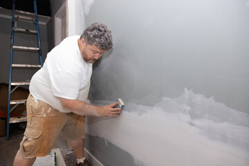 During repair improvement in an apartment room contractor sands wall after putting up putty