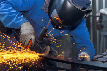 During metalwork workplace in which master grinds metal with grinder sparks are visible throughout...