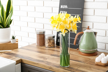 Vase with blooming narcissus flowers on counter in interior of kitchen