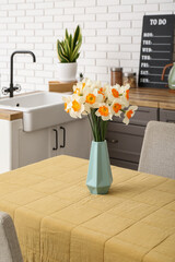 Vase with blooming narcissus flowers on table in modern kitchen