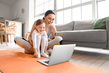 Sporty young woman and her little daughter training with laptop at home