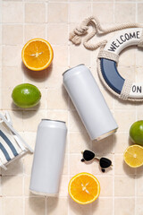Cans of soda with beach decor and citrus fruits on light tile background