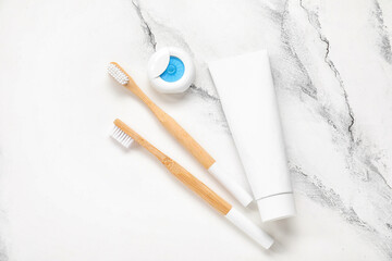 Fototapeta na wymiar Dental floss, paste and bamboo toothbrush on white marble background
