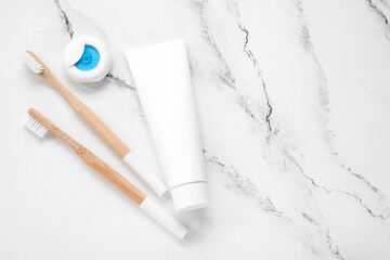 Dental floss, paste and bamboo toothbrush on white marble background