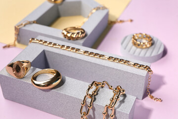 Showcase pedestals with golden rings and bracelets on color background