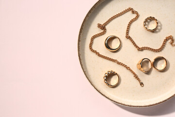 Plate with golden rings and necklace on white background