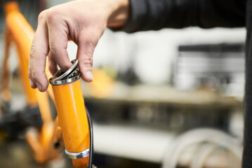 Maintenance of a bicycle: hands of an unrecognizable person disassembling the steering column bearing of an orange bike in his workshop. Selective focus composition with copy space.