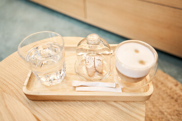 Cup of coffee cappuccino with cantuccini and a glass of water on a wooden tray. Coffee with milk, a cookie and a glass with water on a glass table.