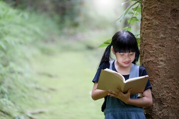 Cute smile asian little girl reading book in garden