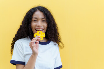 Happy cheerful American - African black woman holding a sliced piece of the yellow bell pepper and smile close up with copyspace on bright yellow background.