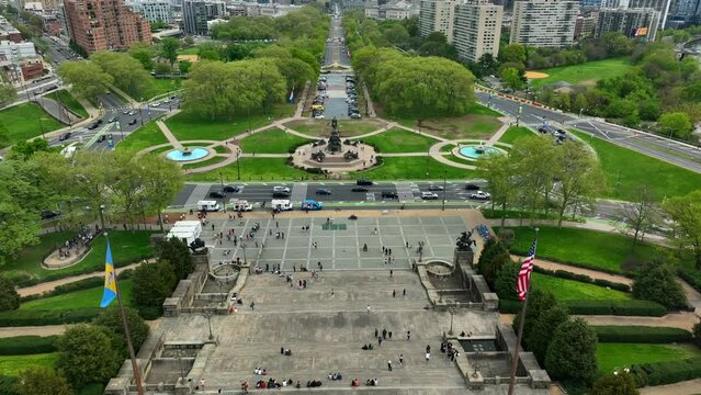 Aerial pan-up of flags on Philadelphia Museum of Art steps, Fairmount Park, City Hall, William Penn Statue, and skyline. Tourists enjoy walkable community and attractions in city of brotherly love.