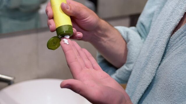 Man Applying Face Cream On Arm While Standind Near Mirror In Bathroom, Close Up