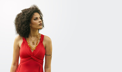 young beautiful brazilian tattooed woman with curly hair wearing red dress, looking to the side and...
