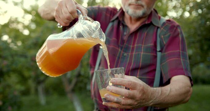 A senior man puring cider into glass at apple orchard