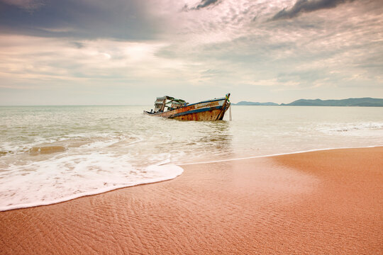 seascape of wreck boat on sand beach with cloudy sky in tropical region season