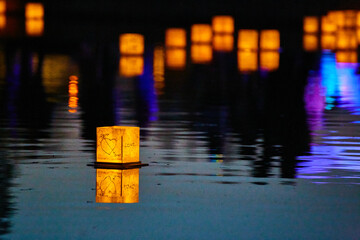Lone lantern on dark pond with neon lights and distant lanterns in background