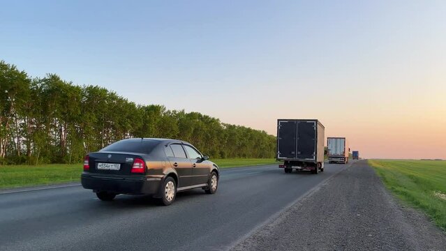 The movement of trucks with a semi-trailer and cars at sunset. Highway traffic. Static view