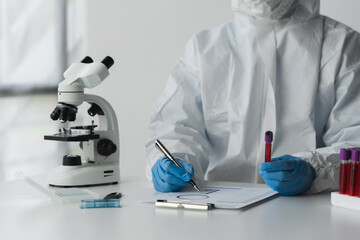 A scientist or microbiologist wearing PPE and a face mask holds a test tube with blood from a patient to create an experimental vaccine. and scientific research to cure vaccine concept.