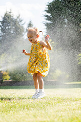 A beautiful girl in a dress plays on a green lawn and splashes with water