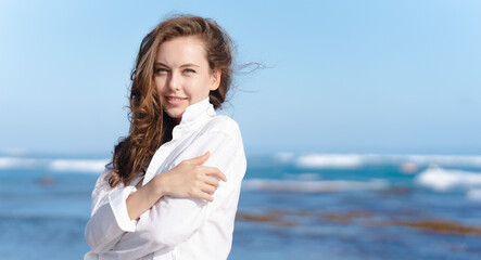 Fototapeta na wymiar A beautiful woman in a white shirt is smiling on the coast of the ocean.