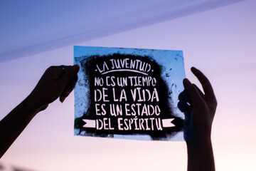 A pair of hands holding a stencil with a phrase about youth.