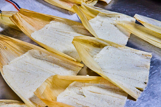 Vertical of silver tray with five pre-baked tamales with masa and corn husk all wrapped up and ready for the oven