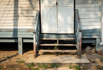 The old worn out wooden stairway with cement base at the entrance door of old wooden building with morning sunlight