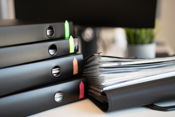 Folder with documents next to a pile of black binders with documents. Colorful stickers on objects....