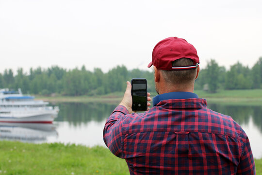 adult man takes pictures on a smartphone of a passenger ship.