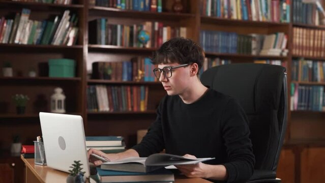 The guy is sitting at the table, typing something on his laptop. He has many books on the table, so he's obviously studying. Occasionally, he gets distracted by external sounds and turns around.