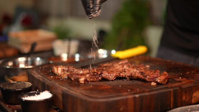 Professional cook salting cooked meat on a cutting board, establishing shot