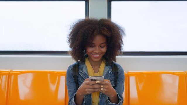 Black young woman, using smart phone and smile in skytrain. Happy african student, young female chatting and typing text message on mobile