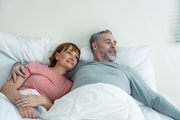Caucasian senior older couple lying down on bed then look at each other.
