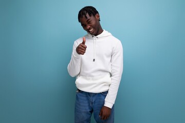 active american young man with dreadlocks in a white sweater inspired shows his hand to the side on a blue background