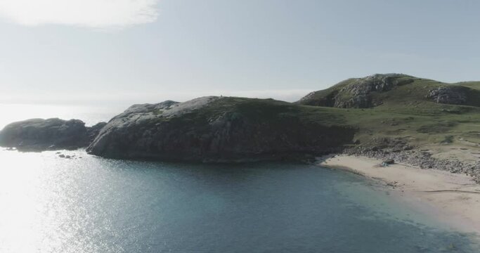 Panning wide drone shot of a white sandy beach with clear blue waters and mountains along the Scotland North Coast 500 Route