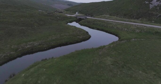 Slow drone reveal of a campervan parked up alongside a river surrounded by hills at dusk in scotland