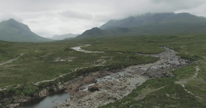 Slow wide drone shot along the Sligachan River on the Isle of Skye with cloud covered mountains in the background