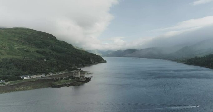 Super wide drone shot of Eilean Donan Castle moving backwards showing the vast mountain and sea view which surronds the castle in Scotland