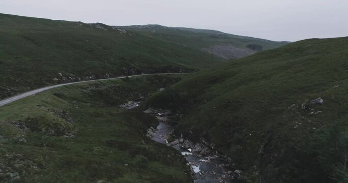 Slow drone pull back revealing a campervan parked up alongside a river and waterfalls surrounded by hills at dusk in scotland