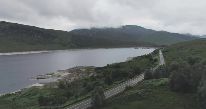 Wide drone shot with a campervan wild camping alongside Loch Beag, BBQ smoke with cloudy mountains in the background in Scottish Highlands