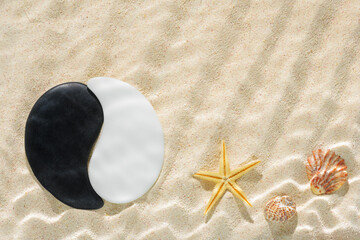 sun lights with hard shadow in wavy water on abstract sand background with shell, starfish and sign Yin-Yang stones, beautiful abstract spa concept