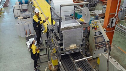Two industrial factory workers working in plant and inspect the machines for metal manufacturing in factory. Manufacturing industry equipment