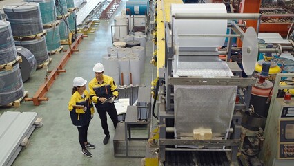 Two industrial factory workers using tablet for working in plant inspect the machines for metal manufacturing in factory. Manufacturing industry equipment
