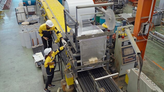 Two industrial factory workers working in plant and inspect the machines for metal manufacturing in factory. Manufacturing industry equipment