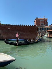 Fototapeta na wymiar Gondel vor der Stadtmauer von Venedig mit Gondoliere auf grünem Lagunen Wasser 