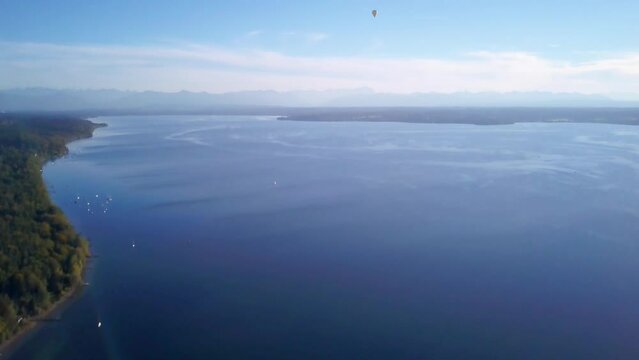 Aerial drone cinematic hot air ballon  fly over sailboats Lake Starnberg Munich Germany Europe at Schloss Seeburg Castle with scenic Bavarian Alps autumn deep blue water forward slowly pan up movement