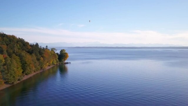 Aerial drone cinematic hot air ballon fly over shoreline Lake Starnberg Munich Germany Europe at Schloss Seeburg Castle with scenic Bavarian Alps autumn deep blue water forward slowly pan up movement